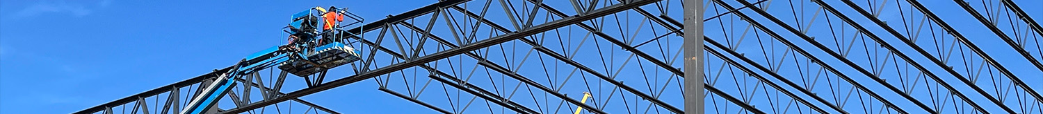view of crane working on steel structure with a blue sky in the background