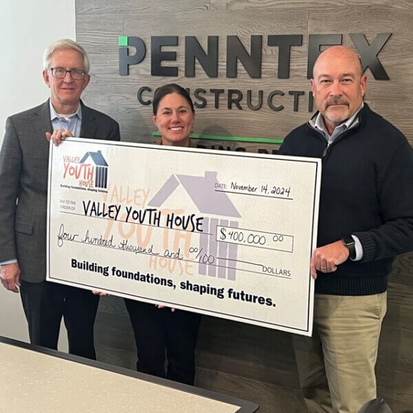 Three people posed with a large donation check
