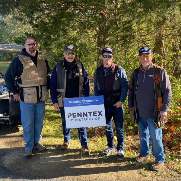 Four people posed with a sponsor sign at an event