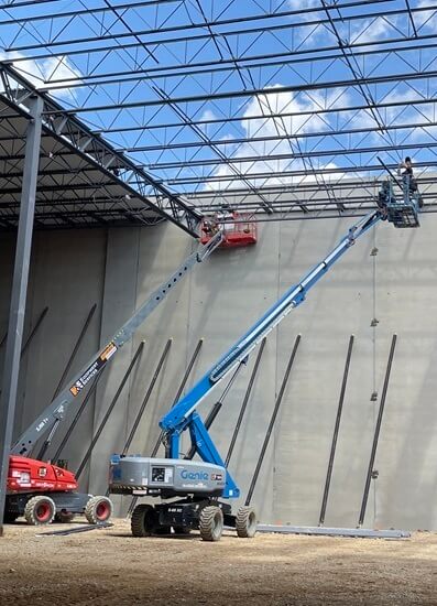 Two lifts with people working on a concrete wall